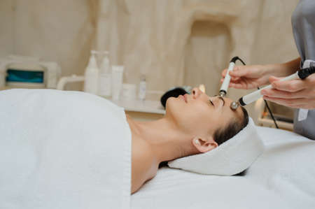 Lateral view of woman facial massage spa procedure. Electric stimulation facial skin care. Microcurrent lift face. Beauty spa procedure. Anti aging rejuvenation non surgical treatment in medical interior roomの写真素材