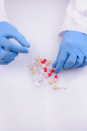 the hands of a doctor holding an ampoule with medicine; pills of different color near itの写真素材