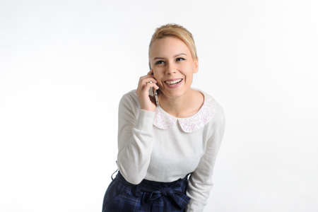 20-years blond girl in white blouse and blue skirt on white background talking on the cell phoneの写真素材