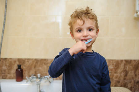 close up photo of a blond boy in blue T-shirt cleaning his teeth in a bathroomの写真素材