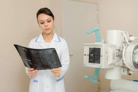 Female doctor looking at patient spinal x-ray in radiologist's cabinet; medical equipment on the backgroundの写真素材