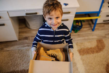close up of a boy holding a open cardboard box with a pair of yellow leatrher bootsの写真素材