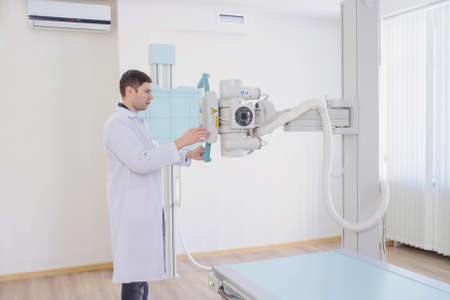 lateral view of a male radiologist adjusting the X-ray machine in examination romの写真素材