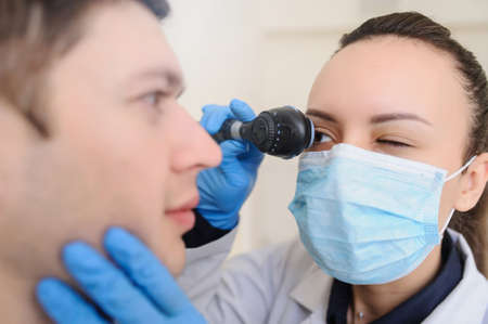 close up photo of a optometrist examining man's eyes with ophthalmoscopeの写真素材