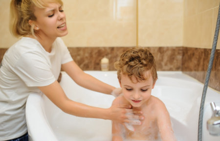 Little boy washing and playing in bathtub with foam and soap bubbles with his mother