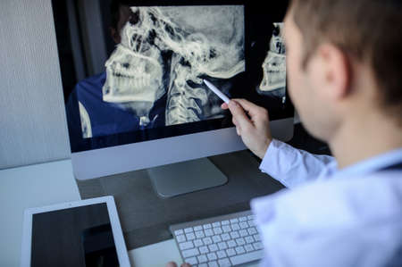 back view of a male radiologist examining neck x-rays (cervical vertebrae) on computerの写真素材