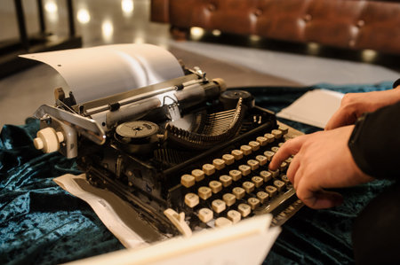 lateral view of man's hand typing on vintage typewriter on a piece of newspaper and dark blue velvet...