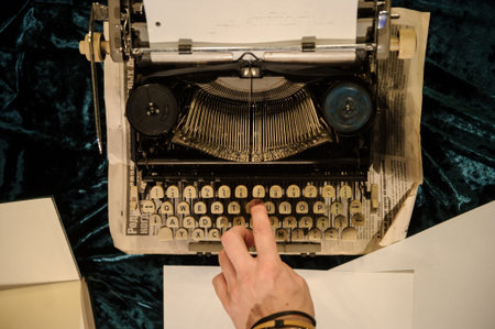 top view of man's hand typing on vintage typewriter on a piece of newspaper and dark blue velvet...