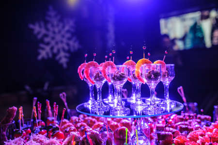 Buffet table with snacks, canapes; shrimp with sauce in glasses at a birthday party in blue lightsの写真素材