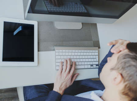 back view of a young man sitting in front of a computer monitor and thinking about a taskの写真素材