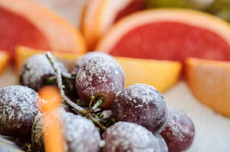 close up photo of mix of fruits on the plate: grape with powdered sugar and sliced grapefruit