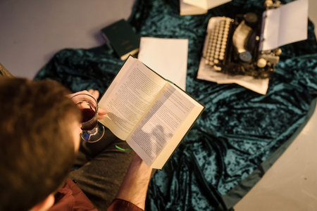top view of man with a book in his hands sitting near a vintage typewriter on a dark blue velvet...