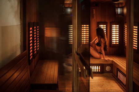 lateral view of a beautiful lady in back bathing suit having spa procedure in a wooden saunaの写真素材