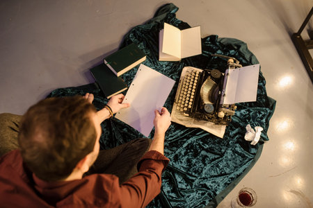 top view of man with a piece of paper in his hands sitting near a vintage typewriter on a dark blue...