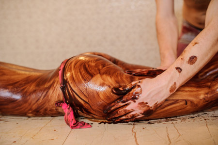 lateral view young woman having a chocolate massage on her ass and legs done by a man