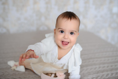 close up photo of a cute baby girl in a white dress on a gray blanket at home