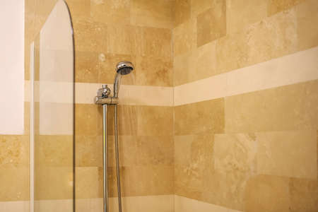 Water running from shower head in bathroom on a light brown background behind a glass wallの写真素材