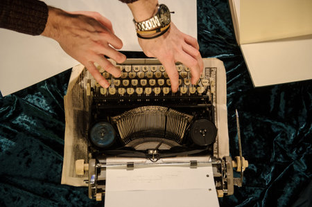 top view of man's hands typing on vintage typewriter on a piece of newspaper and dark blue velvet...
