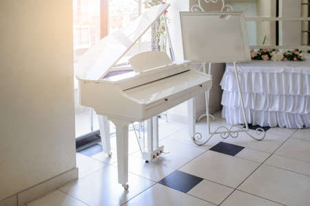 white piano in a restaurant hall near a white table decorated with flowersの写真素材