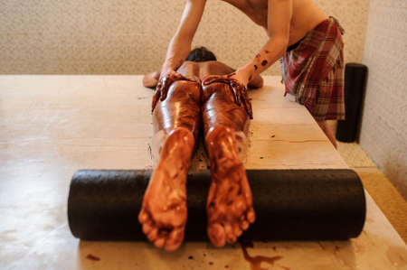 close up photo of young woman having a chocolate massage on her ass and legs down by a manの写真素材