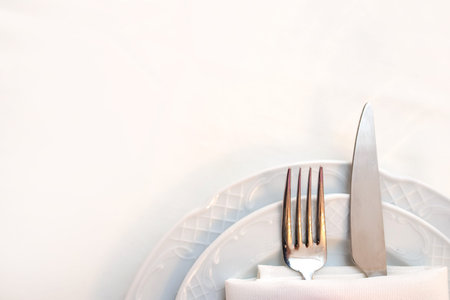 close up photo of knife and fork in a folded napkin on two plate