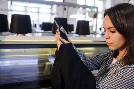 lateral view of a young woman analyzing a knitted piece of cloths near industrial knitting machine...