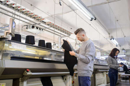 close up photo of a young man analyzing a piece of clothes and a woman working on industrial knitting machineの写真素材