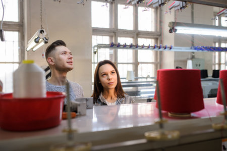 close up photo of a young woman and man looking and discussing near a industrial knitting machine...