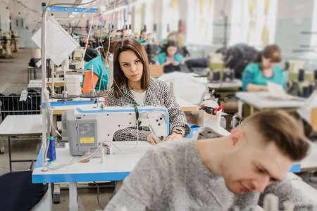 close up photo of a young man and other seamstresses sewing with sewing machine in a factoryの写真素材