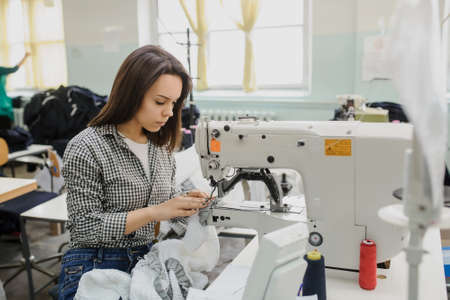 close up photo of a young woman sewing with sewing machine in a factoryの写真素材
