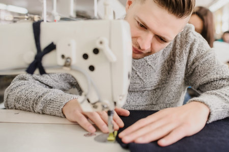 close up photo of a young man sewing with sewing machine in a factory