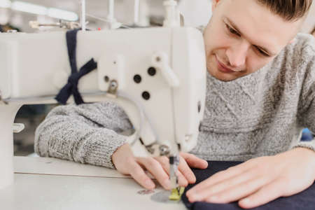 close up photo of a young man sewing with sewing machine in a factoryの写真素材