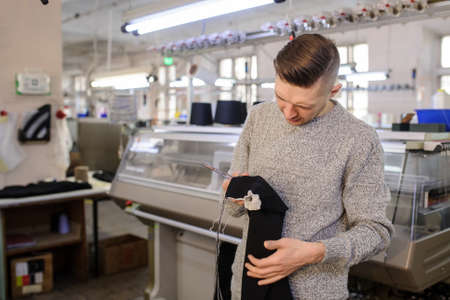 a young man analyzing a knitted piece of cloths near industrial knitted machines with black thread in conesの写真素材