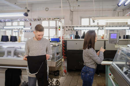 close up photo of a young man analyzing a piece of clothes and a woman working on industrial knitting machineの写真素材