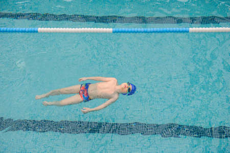 top view of a 7-year boy swimming backstroke in a swimming poolの写真素材
