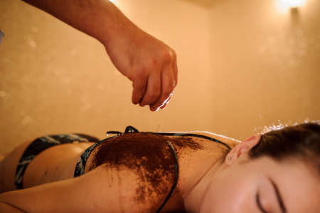 lateral view of a beautiful woman in spa salon having spa therapy with coffee done by a masseurの写真素材