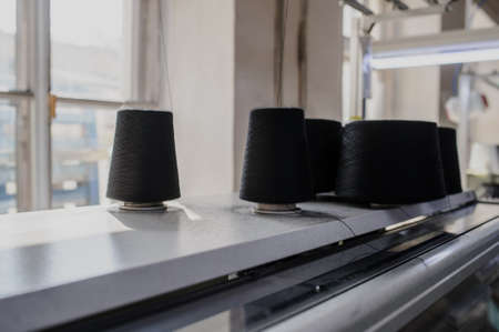 close up photo of black threads in cones on the industrial knitting machine in a factoryの写真素材