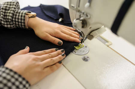 close up photo of the hands of a young woman sewing with sewing machine in a factoryの写真素材