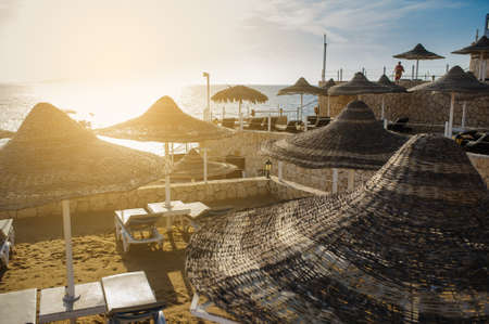 Thatched beach umbrellas and loungers on a beach at an idyllic tropical resort for a summer vacationの写真素材