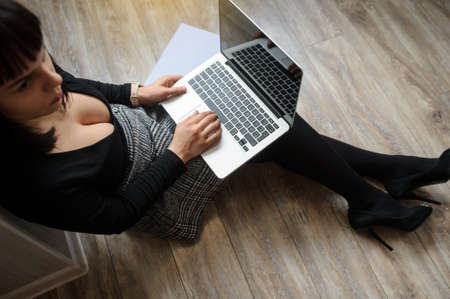lateral view of a hot brunete in office outfit sitting on the floor and working on computerの写真素材
