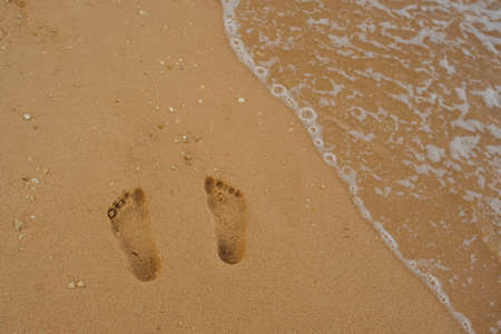 Footprints of human feet on the sand near the water on the beachの写真素材
