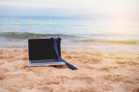 close up photo of a laptop on the beach with a tie on it