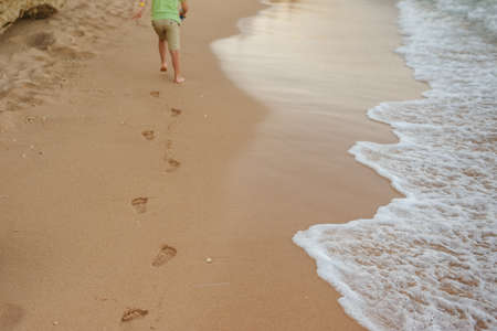 little boy walking on the beach and leaving footprints in the sandの写真素材