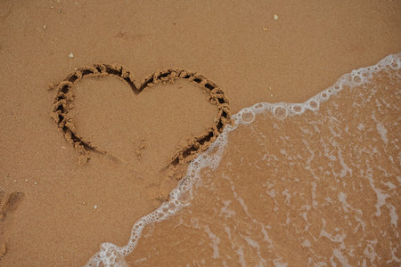 top view heart drawn on the sand of a beach with wave and sunlight