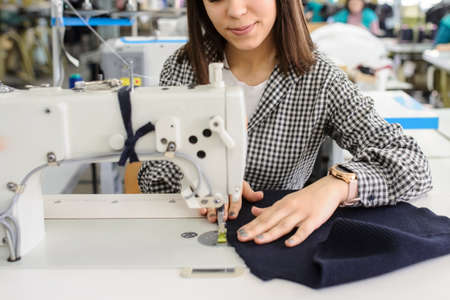 close up photo of a young woman sewing with sewing machine in a factoryの写真素材