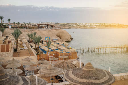 Thatched beach umbrellas and loungers on a beach at an idyllic tropical resort for a summer vacationのeditorial素材
