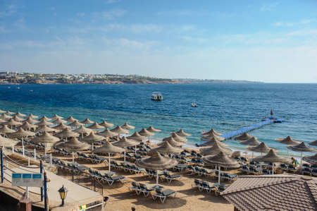 Thatched beach umbrellas and loungers on a beach at an idyllic tropical resort for a summer vacationのeditorial素材
