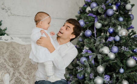 Father holds in his arms his little baby daughter near a christmas tree.の写真素材