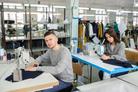 close up photo of a young man and other seamstresses sewing with sewing machine in a factoryの写真素材