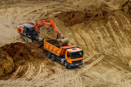 Industrial truck loader excavator moving earth and unloading into a dumper truckの写真素材